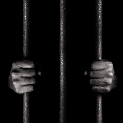 Black & white photo of hands grasping prison bars